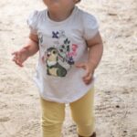 child in white crew neck t-shirt and yellow pants standing on brown sand during daytime